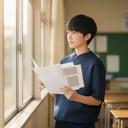学校の窓辺で資料を手に、授業の案内を読む学生